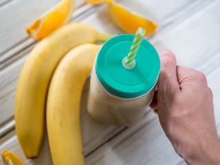 Glass jar with banana and orange smoothie in hand
