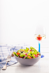 Fresh greek salad served in bowl with glass of white wine.