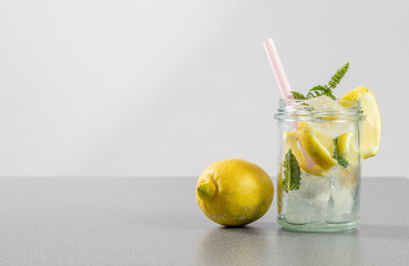 Frische Zitrone neben einem Glas mit selbstgemachter Zitronenlimonade auf einer grauen Arbeitsplatte in der Küche