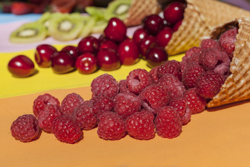 Scattered fruits (strawberries, pineapple, raspberries, kiwi, blackberries, cherries) in waffle, cone cups on a bright colored background