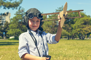 The concept of a dream is to become a pilot, boy in the form of an aircraft pilot ; Happy child In a helmet with glasses and binoculars, playing with toy airplane . toned