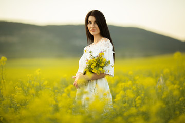 Pretty woman with bouquet of wildflowers in yellow field in sunset lights, summer time