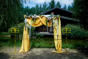 Arch for wedding ceremony in the open air, decorated with yellow fabric and flowers.