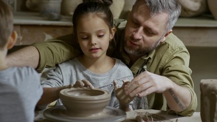 Cinemagraph of bearded man and his little daughter forming bowl out of clay spinning on pottery wheel in workshop