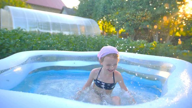 Little girl is swimming and jumping in the garden pool