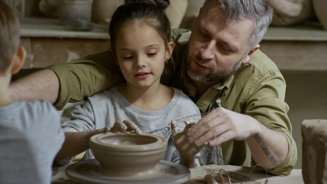 Cinemagraph of bearded man and his little daughter forming bowl out of clay spinning on pottery wheel in workshop