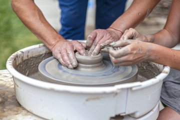 pottery training, a close-up of a woman potter teaches a man how to properly mold a bowl of brown clay on a potter
