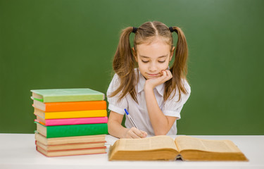 Little  girl with book preparing for the exam on the background of a school board