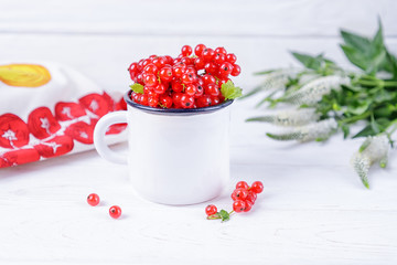 Ripe red currant berries in a white cup and flowers on a white background