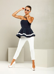 Fototapeta premium Beautiful and attractive model dressed in expensive clothes. White pants, navy blue blouse and high heels. A photo of a fashion shot in the studio.