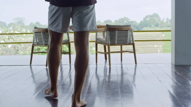 Caucasian man with messy hair stretching arms and shoulders when enjoying fresh air on balcony after waking up in the morning