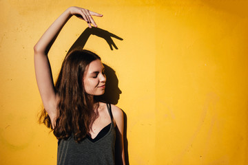 Young teen girl dancing outdoors on yellow wall background in urban area