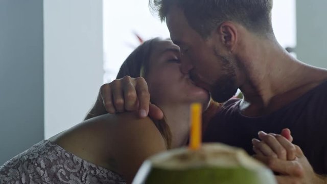 Medium shot of passionate Caucasian couple sitting at table when having breakfast, kissing and smiling, woman lying on man&rsquo;s chest