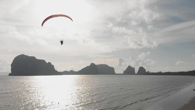 Para motor flies along the sandy beach over the sea. Background with islands view. The coast of Thailand. Trang province. Sikao. Paraglide. Paramotor.