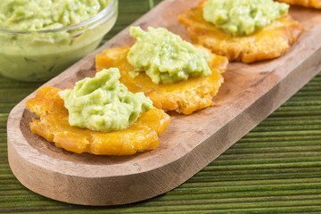 Patacon fried pieces of crushed green banana. Guacamole. On the wooden table (toston, tachino)