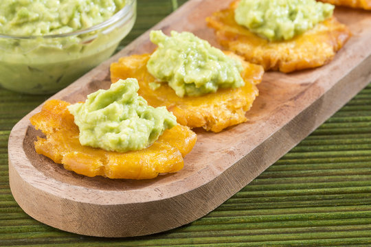 Patacon fried pieces of crushed green banana. Guacamole. On the wooden table (toston, tachino)