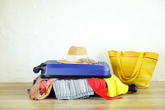 Close Up Of Clothes Don't Fit In Messy Fully Packed Closed Suitcase, Things Sticking Out. Blue Hard Shell Luggage. Beach Bag, Hat, Sunglasses. Woman Packing For Vacation Concept. Copy Space Background