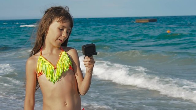 A child at sea with a video camera. A little girl on the beach takes pictures of herself on a video camera.