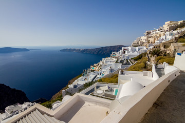 Terrace with view, incredibly romantic scene, Santorini. Fira, Greece. Amazing daytime cityscape towards Oia and the deep sea crystal waters with white houses and swimming pools