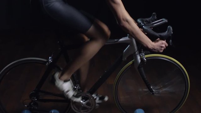 Tilt up of fit professional athlete in protective helmet and sunglasses cycling on rollers against black background