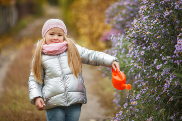 Little girl watering the flowers in the garden in the autumn