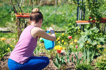 Caucasian young woman watering flowers with water can at a household plot. Back view.