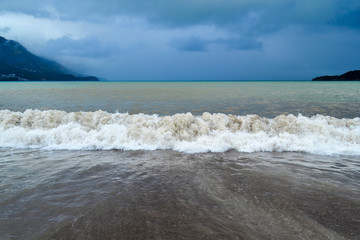 Sea wave in stormy weather. The turbid wave. Low clouds over the coast. Montenegrin beach in rainy weather. The sea and mountains of Montenegro. Budva. Becici