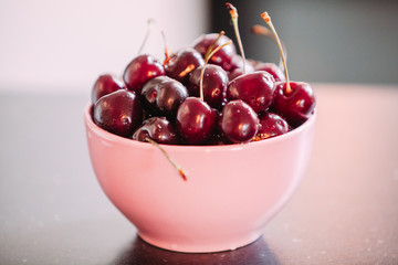 Pink Bowl of fresh red cherries on colorful background - side view.