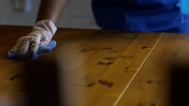Mid-section shot of hands of unrecognizable female housekeeper in gloves and uniform washing dinner table with sanitizing spray
