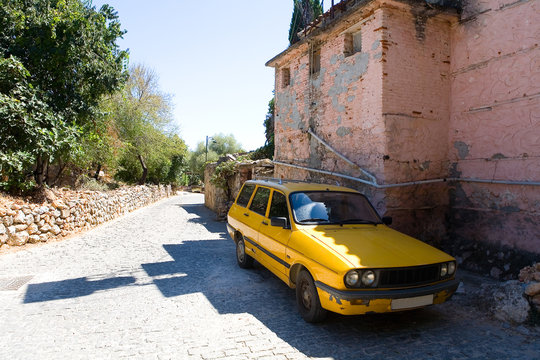An old yellow French car stands near the old building.