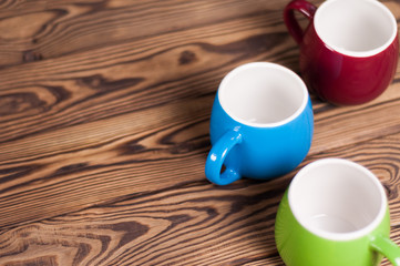 Three colored empty ceramic clean mugs on old worn brown wooden table with copy space