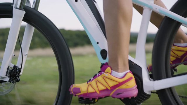 4K sport footage, close up female legs shoes standing electric mountain bike cycling down trail in rural landscape
