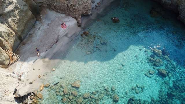 Aerial drone bird's eye view of iconic volcanic white chalk beach and caves of Tsigrado with turquoise and sapphire clear waters, Milos island, Cyclades, Greece