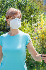 Woman in protection mask holding bouquet of wildflowers and trying to fight allergies