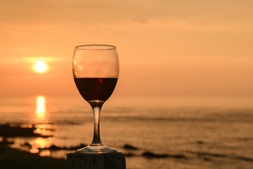 Red Wine. A wine glass half full of wine on a wooden post with the sun setting over the Pentland...
