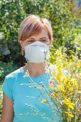 Woman in protection mask holding bouquet of wildflowers and trying to fight allergies