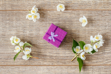 Small gift box wrapped with violet ribbon on wooden boards decorated with flowers of jasmine