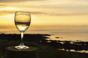 White Wine. A wine glass half full of wine on a wooden post with the sun setting over the Pentland Firth, Caithness, Scotland.