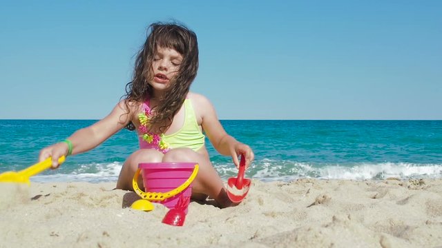 A child is playing with sand on the beach. Little girl is pouring sand into a bucket on the beach by the sea.