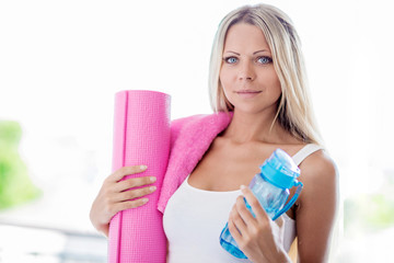 Young blonde woman going fitness sport with towel, bottle of water and yoga mat