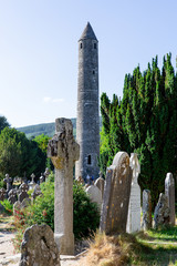 Stone round tower surrounded by gravestones at the monastic site in Glendalough Valley in county...