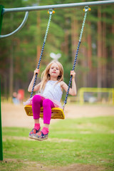 Little blonde girl smiling swinging outdoors on a playgroung