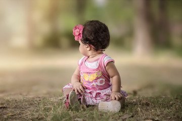 Baby girl sitting outside on green grass and looking into the distance, selective focus. shallow depth of field.