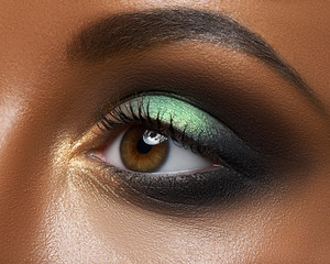 Macro and close-up creative make-up theme: beautiful female eye with green and golden shadows, black skin - obrazy, fototapety, plakaty