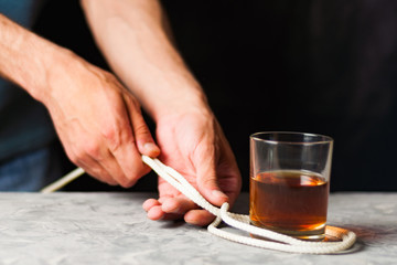 Man ties transparent glass and alcohol with rope on gray cement on black background