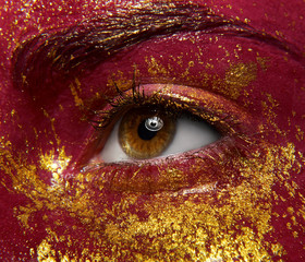 Macro and close-up creative make-up theme: beautiful female eyes with liquid red paint and gold sparkles