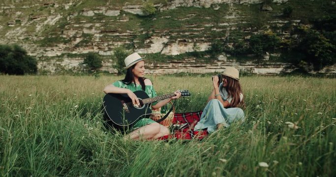Picnic time with two girls , who singing at guitar and second girl making pictures, they happi smiling. 4k