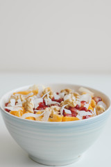 Vertical photo of fruit salad with pomegranate seeds, mango slices, fried apricot, coconut flakes, banana, tangerine and walnut. Healthy breakfast. Nutrition concept