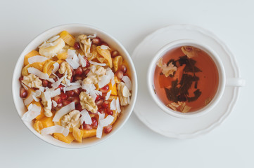 Red Hibiscus tea and fruit salad with mango, coconut flakes, walnut, tangerine, dried apricot, banana and pomegranate seeds on white table, top view