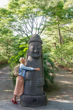 Caucasian Female Tourist Hugging Dol hareubang, also called tol harubang, hareubang, or harubang - Traditional Statue Guard of Jeju Island in South Korea. Sculpture Made of Volcanic Rock